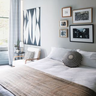 Light grey coloured bedroom with bed with white bedding, throw, and cushion, hanging wall art and chair