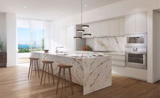The kitchen has a large marble island with three wooden stools in the centre and a fitted kitchen to the right.