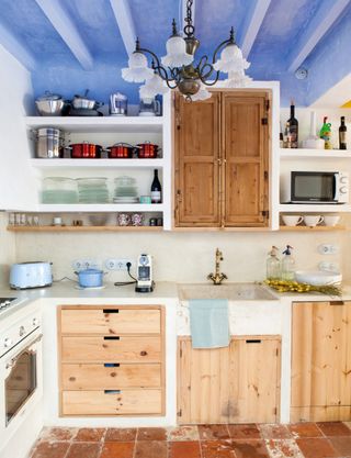 Kitchen with stripped back wooden cabinets with blue painted ceiling and open shelving