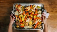 Tray of roasted veg held by hands using dish clothes instead of oven gloves