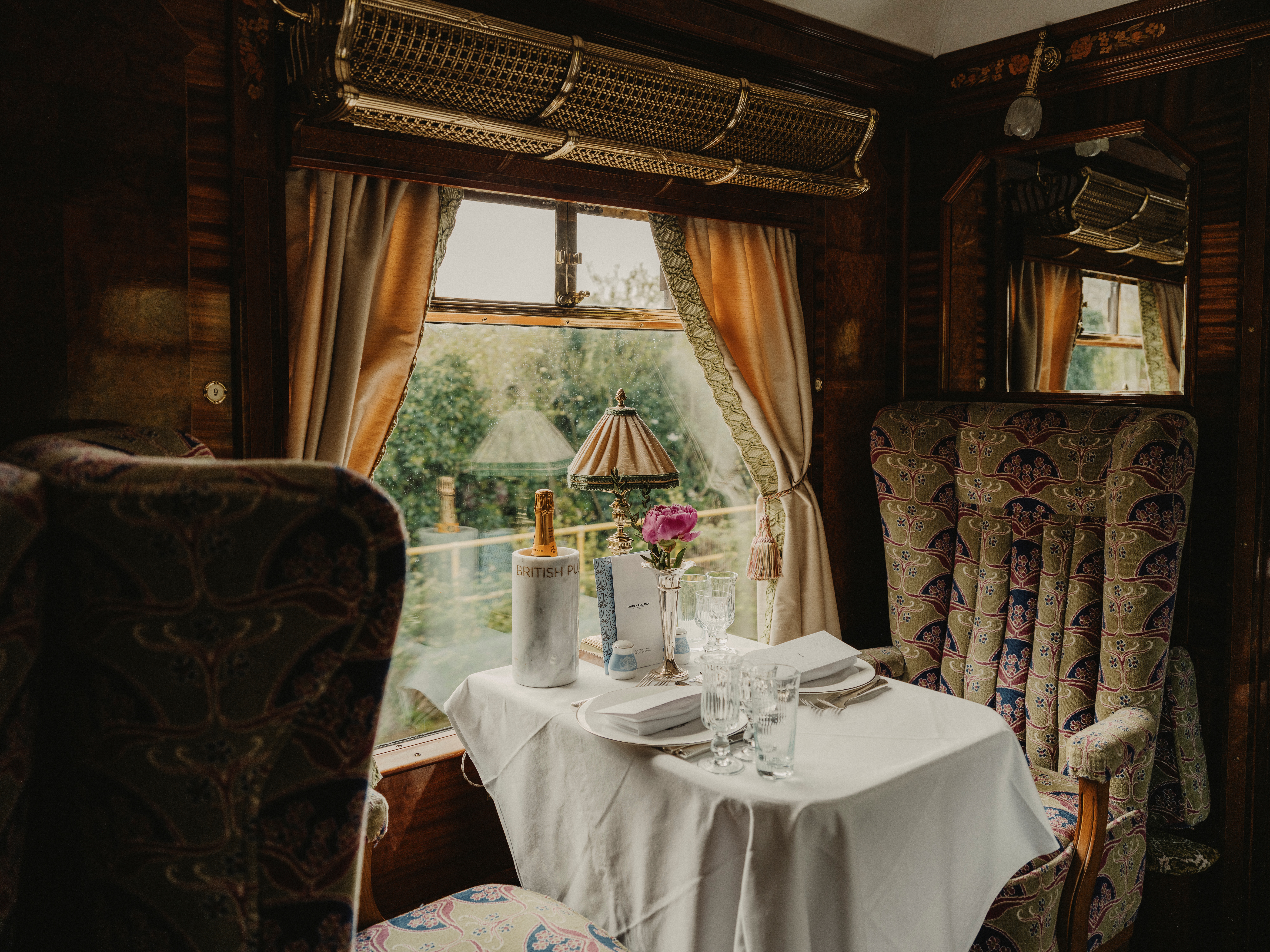 A historical train carriage with upholstered purple, green, and cream seats and marquetry-covered walls with floral motifs.