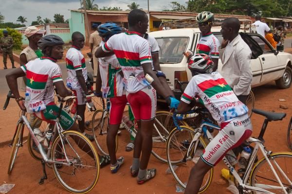 The Burkina team, resplendent in matching uniforms and modern bikes, holds a meeting with their coach prior to the start