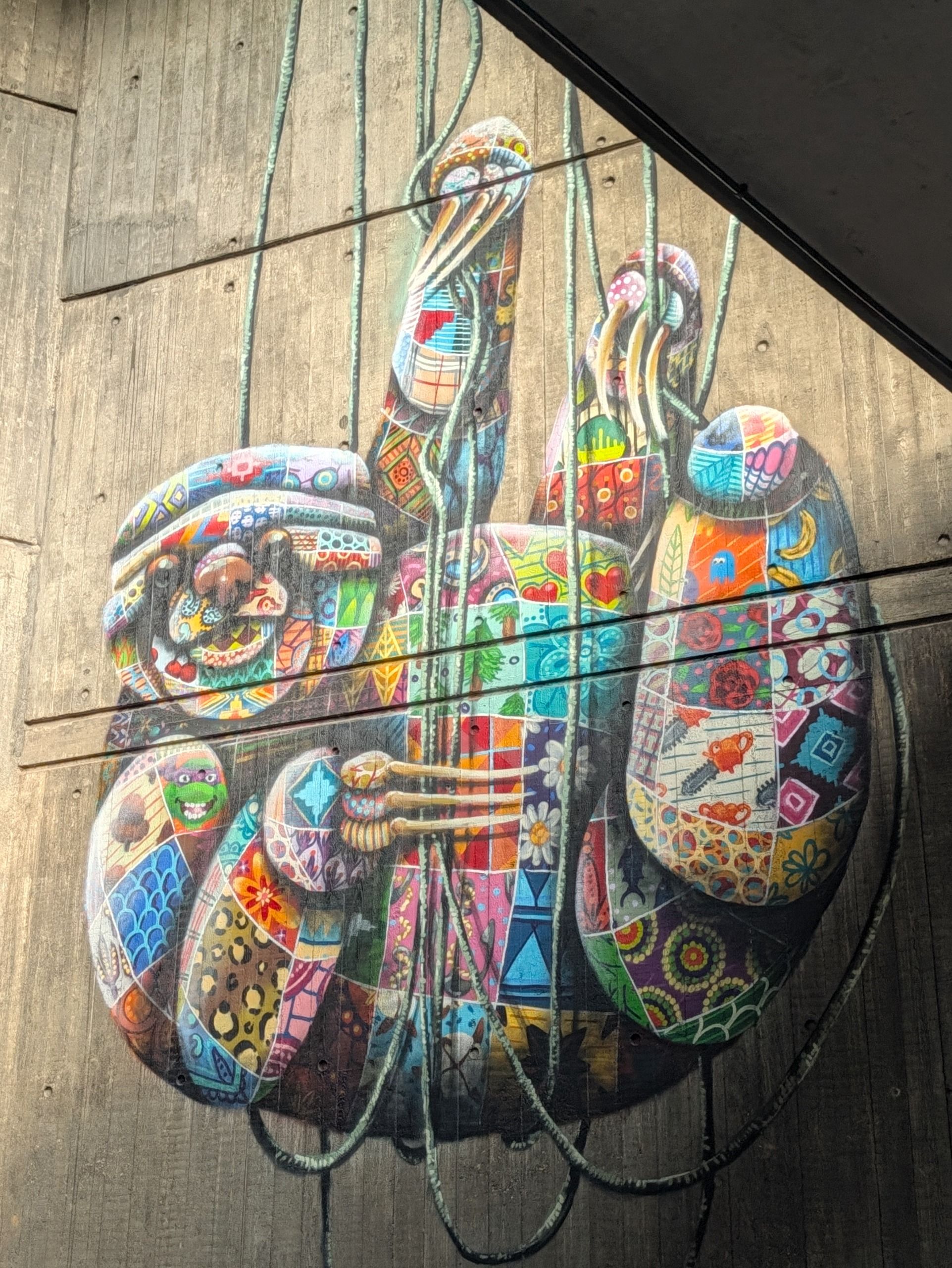 Colorful mural of stylized figures painted on a concrete wall beneath an overpass.