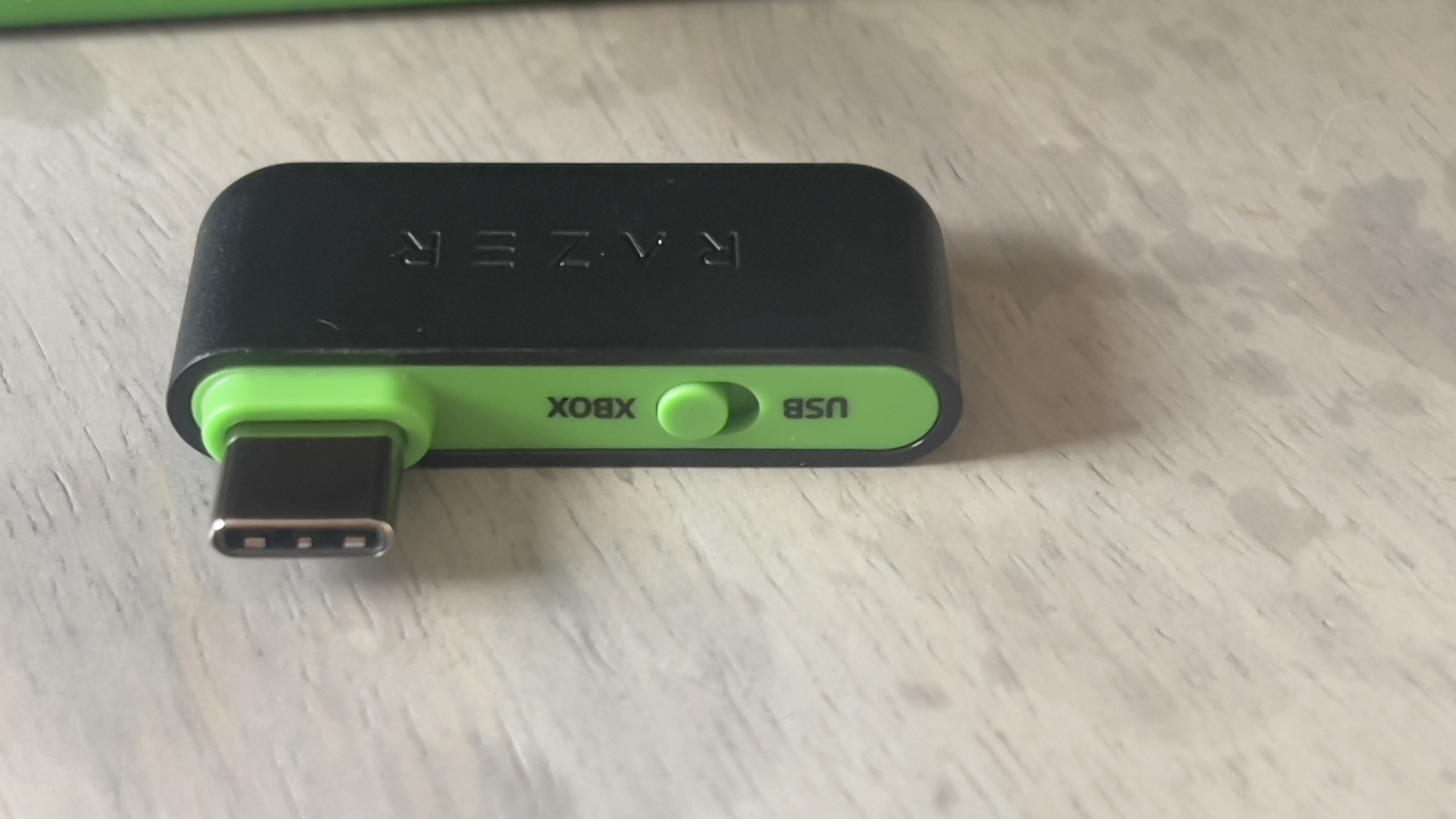 The Razer Blackshark V3 X gaming headset on a table. A living room is visible in the background.