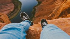 Feet of a man dangling over the edge of a cliff as he sits at the edge
