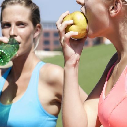 Fit women with pre-workout snacks (drinking water and eating a pear)