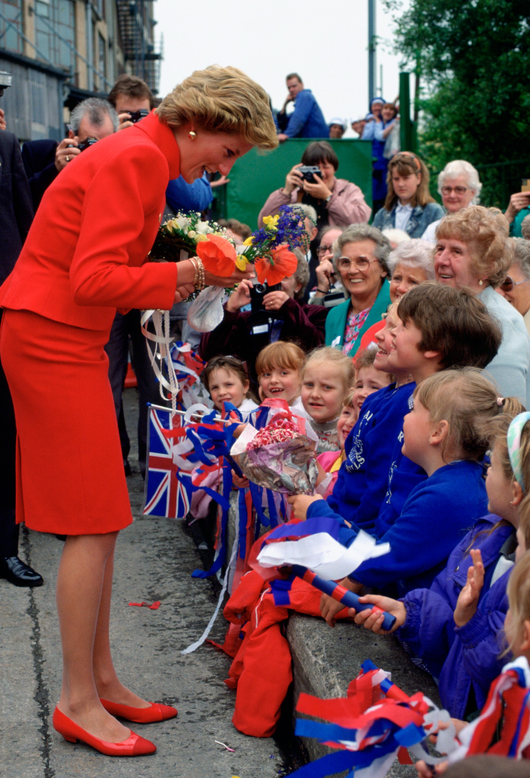 Princess Diana wearing a red suit bending forward and talking to fans