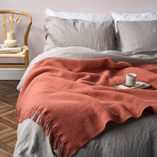 A double bed dressed with grey linen sheets and a cosy terracotta waffle blanket