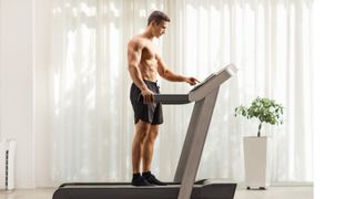 Muscular man standing on treadmill during home workout