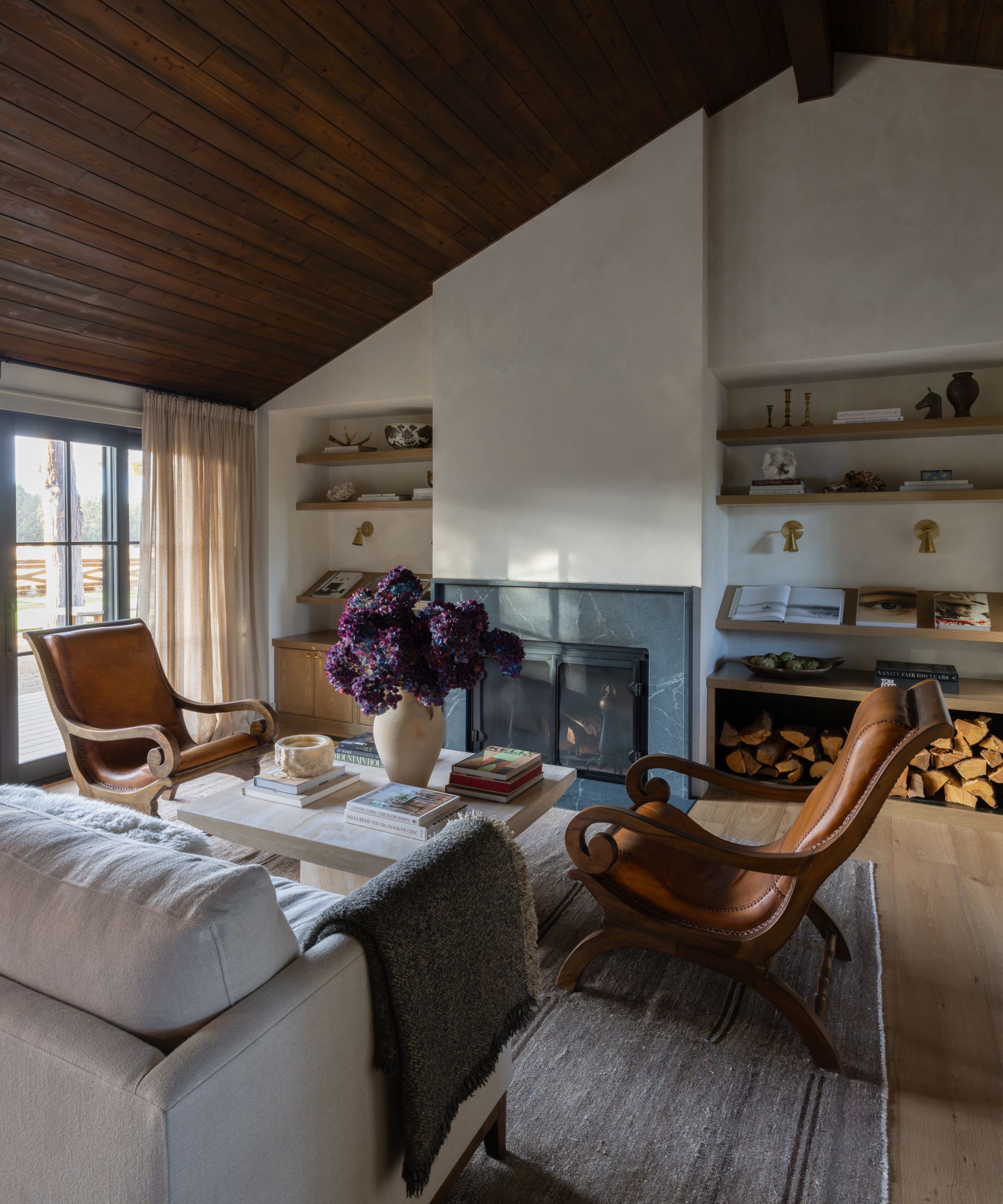 Cozy living room with a fireplace, leather armchairs, and a vase of dark purple flowers on a coffee table.