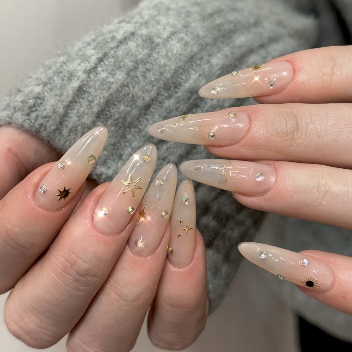 A long nude jelly manicure with gold starburst and galactic motifs.