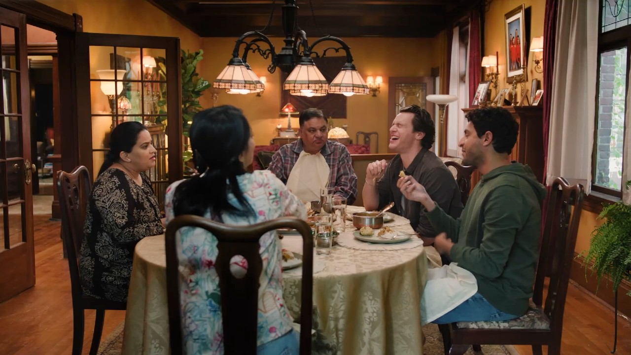 Jonathan Groff laughing around the table with Karan Soni, Harish Patel, Zarna Garg, and Sunita Mani in A Nice indian Boy.