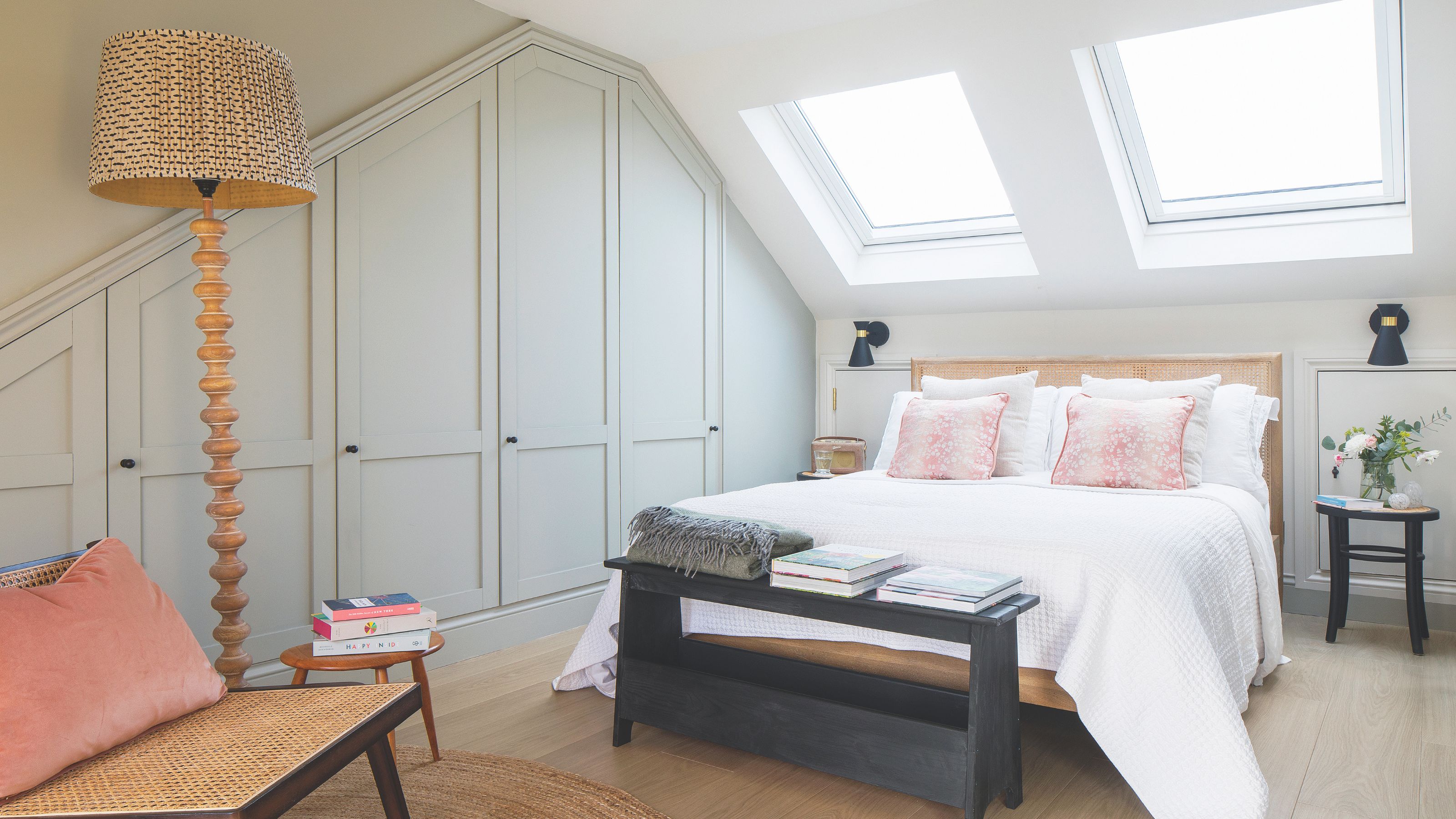 Loft bedroom with fitted grey wardrobes on the left and the bed sitting under a skylight in the middle