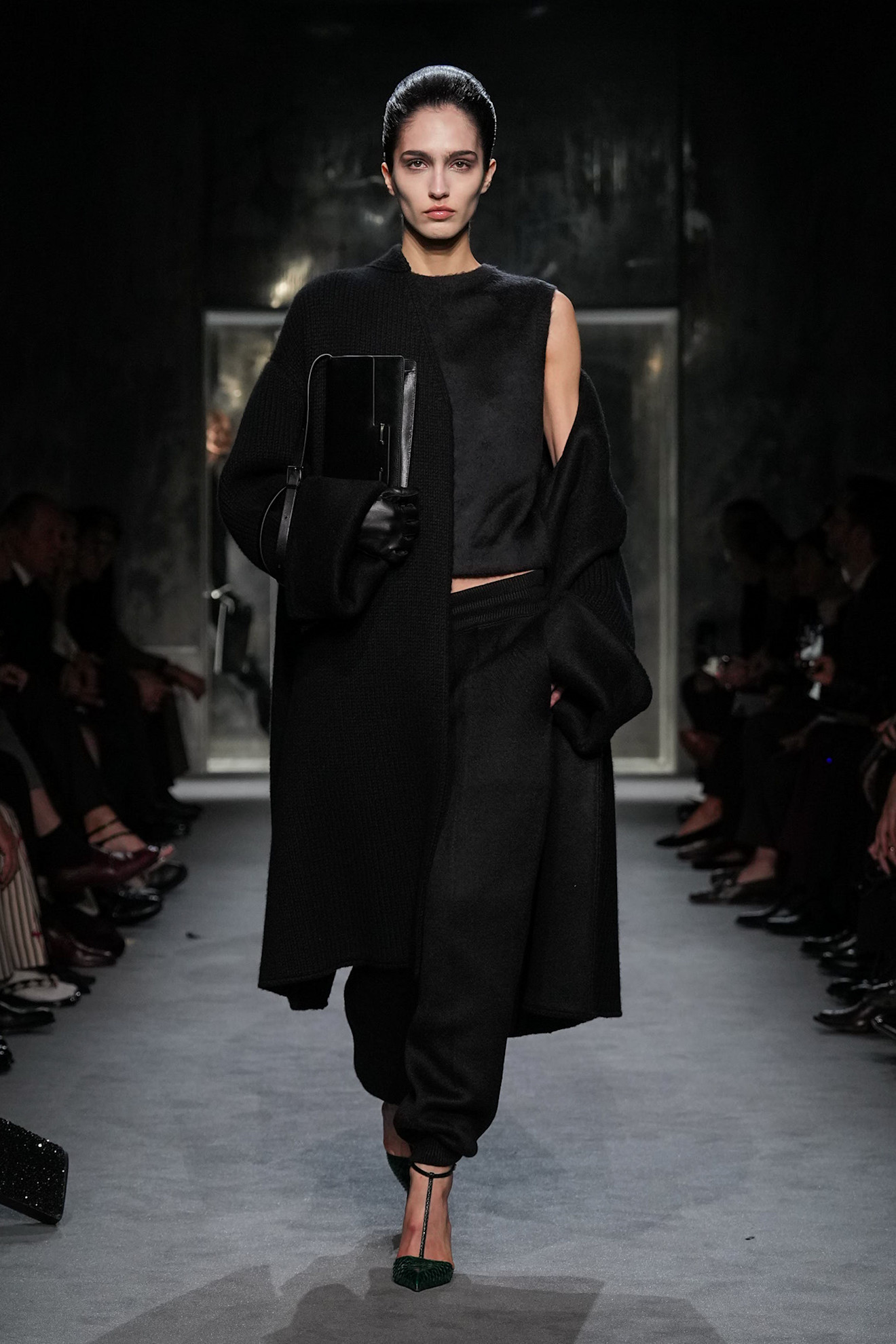 A model wearing a black coat and lounge pants walking in Haider Ackermann's first Tom Ford runway show during Paris Fashion Week.