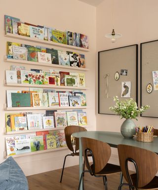 Playroom with pink walls, table with wood chairs, wall of childrens books and two noticeboards