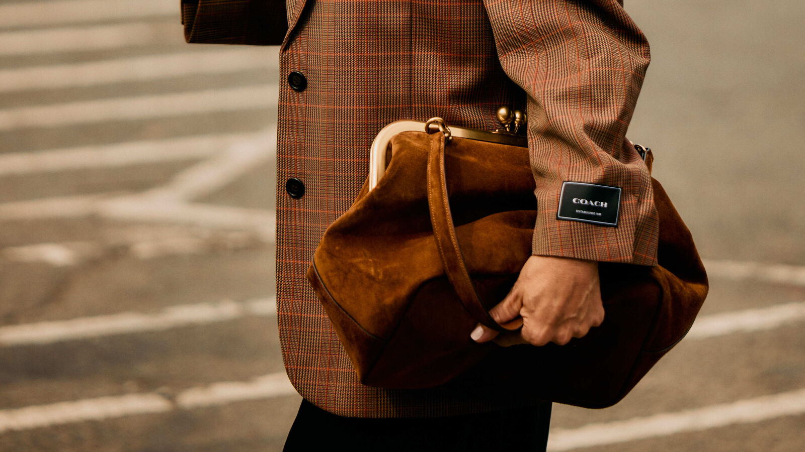 Woman wears brown suede or brown leather while holding a coach bag. 