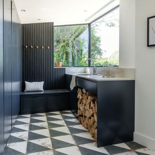 Black and white utility room with tiled floor, wood panelling, coat pegs, built-in bench, marble basin and wood store