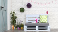 Outdoor pallet furniture in a bench style, painted in a pastel blue with cushions by a wall
