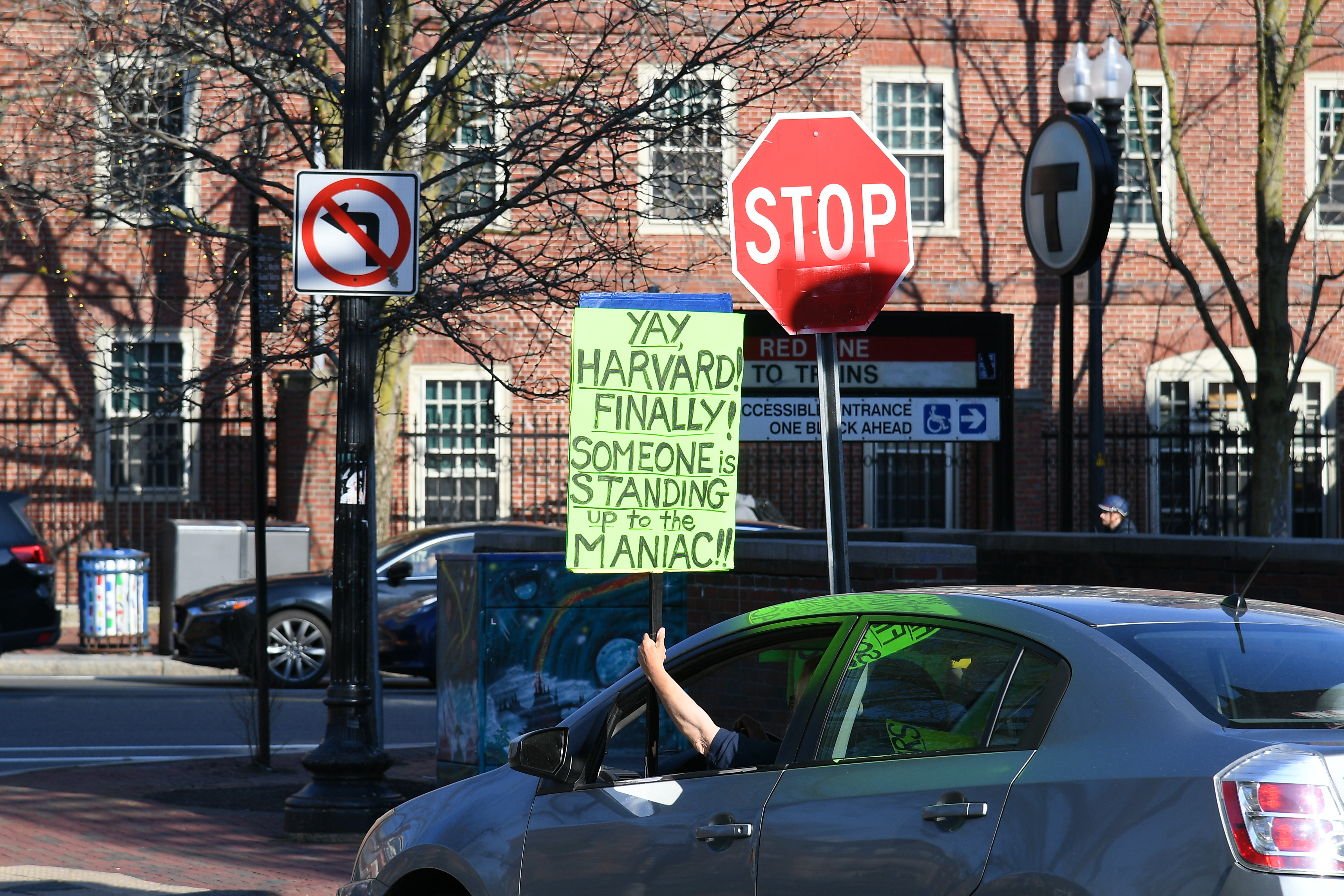 CAMBRIDGE, MA - March 15: A person holds up a sign from their car regarding President Trump and Harvard University on April 15, 2025, in Harvard Square in Cambridge, MA. 