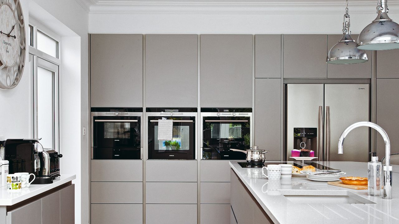 Full height kitchen units in light grey colour and eye level integrated ovens in a renovated kitchen diner