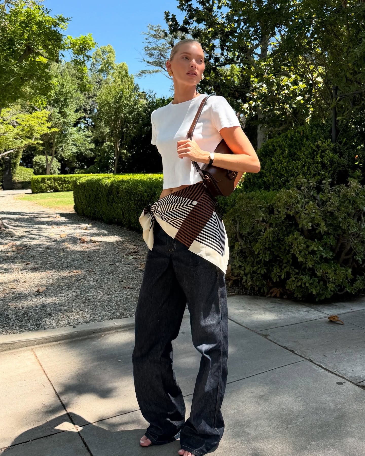 Elsa Hosk wearing a cropped white T-shirt, waist scarf, dark denim jeans, and a brown Gucci bag