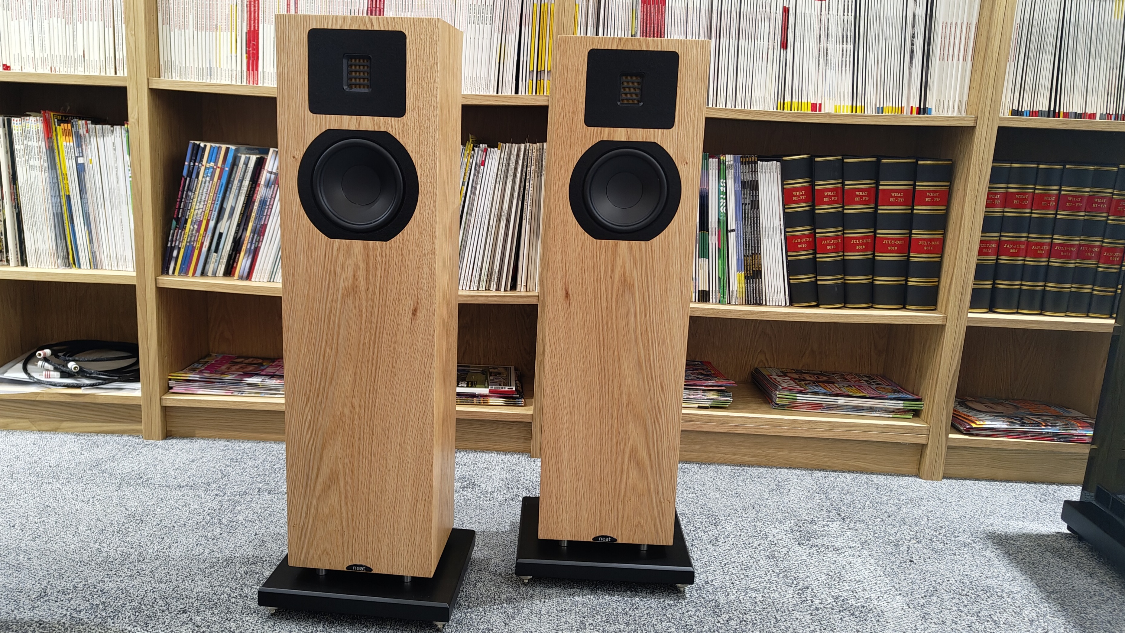 Neat Mystique Classic floorstanders in front of a bookshelf