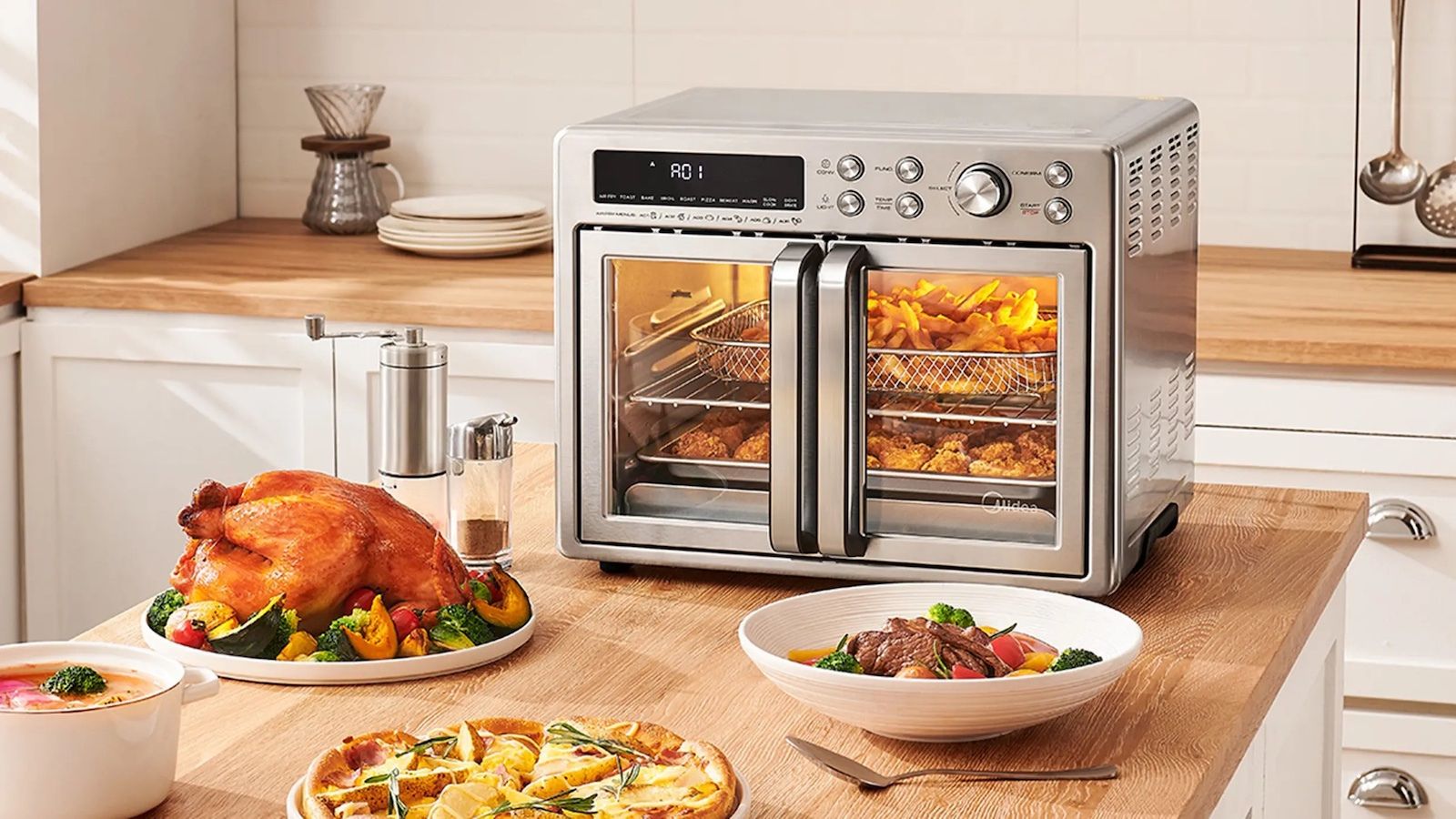 Midea Flexify French Door Air Fryer Oven on a kitchen island surrounded by roast chicken and pizza dishes