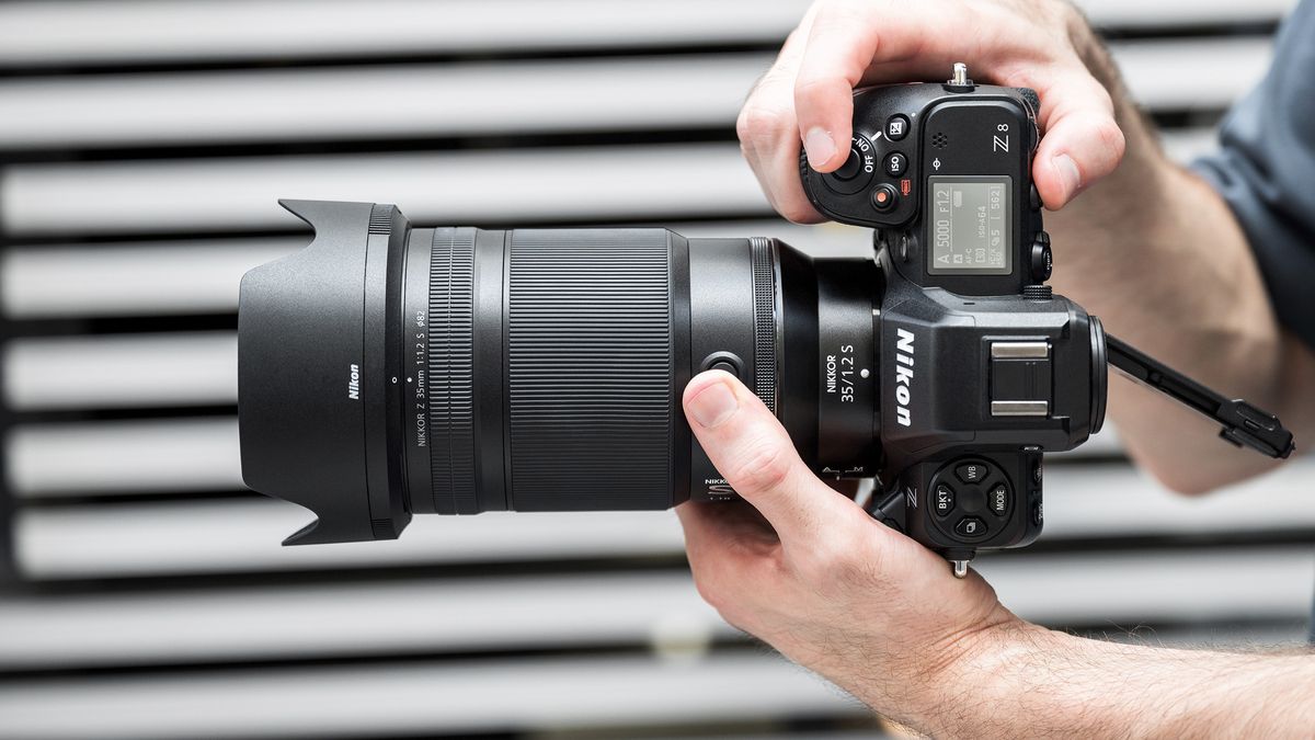 Nikon Z 35mm f/1.2 S in the hand in front of gray slatted backdrop