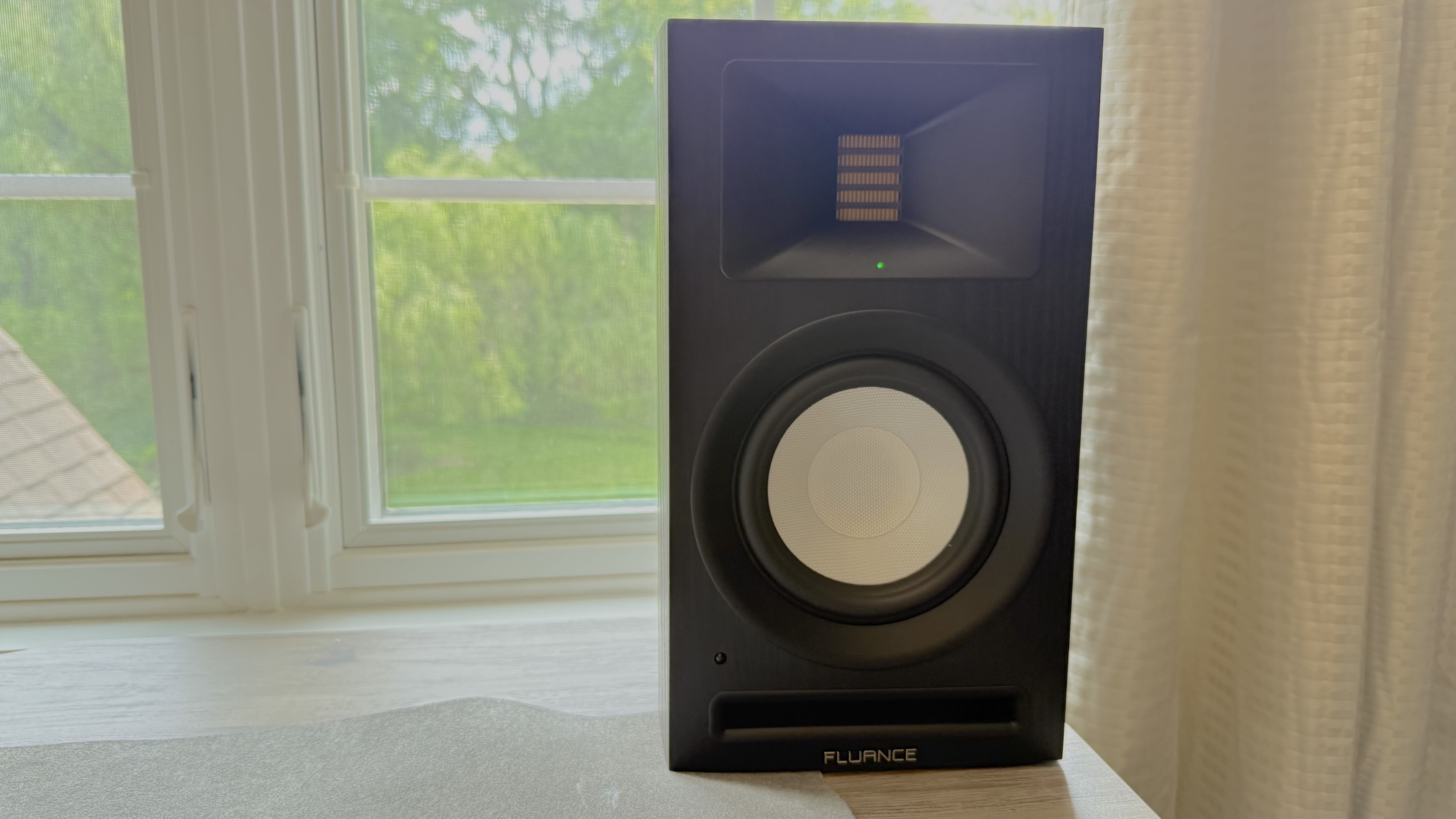 Fluance Ri71 speaker on a windowsill, with the 'power on' button illuminated green.