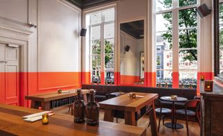 Bar with lower-half of walls in vibrant orange. Dark wood tables and chairs and mirrors beside the windows