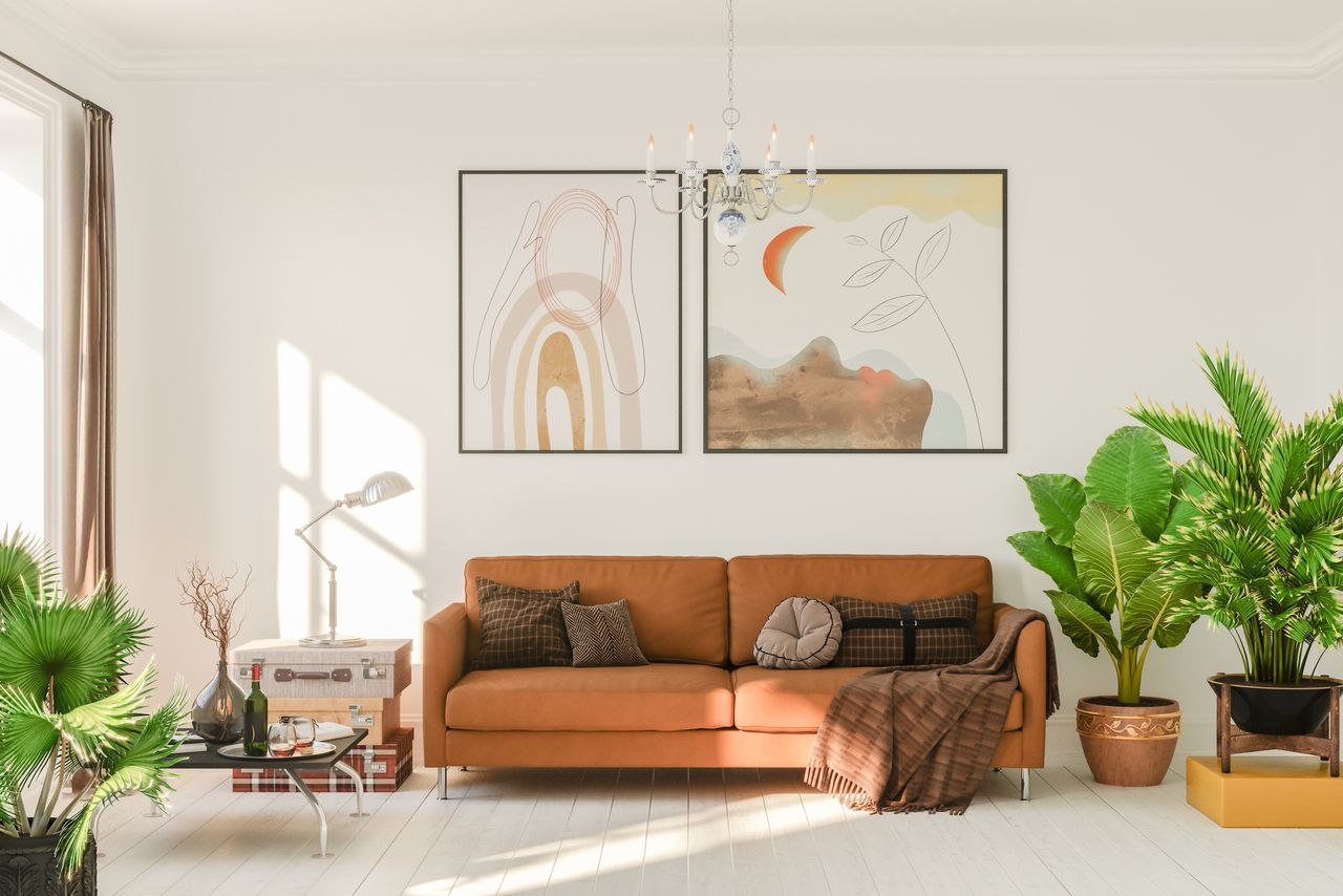 A living room with plants, a sofa, cushions and some wall art