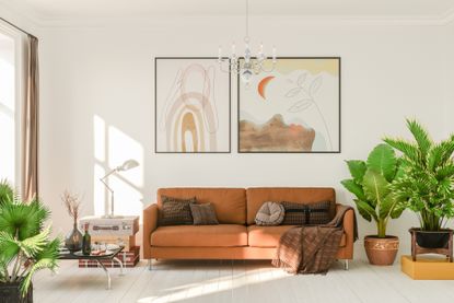 A living room with plants, a sofa, cushions and some wall art