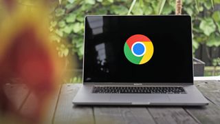 A photo of the Google Chrome logo on a black background, displayed on the screen of a large MacBook Pro which is situated on a table with green foliage behind.