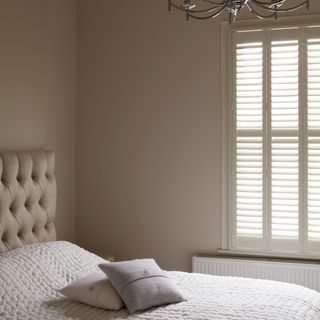 A neutral bedroom painted in Farrow & Ball's Skimmin Stone with a tonal quilted headboard