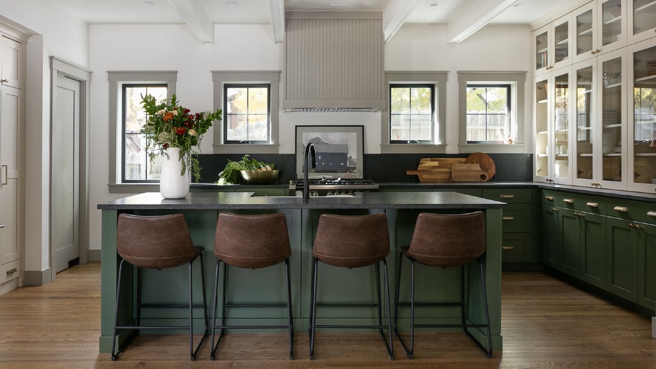 forest green kitchen with black quartz countertops, hardwood floor, leather bar stools, glazed counter units, black faucet, island with sink