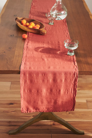 orange table runner running off the edge of a wooden table with glassware and fruit bowl on top