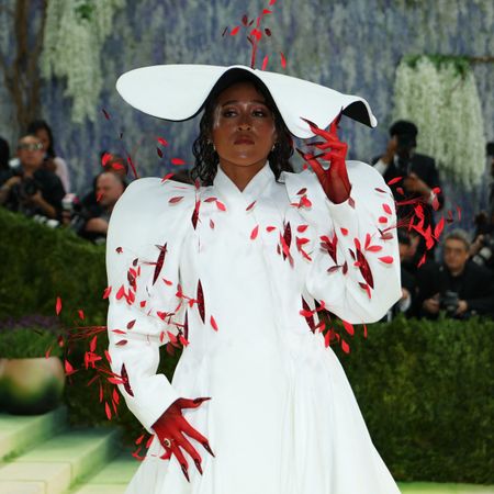 a woman attends the met gala in a long, white coat and a white hat with red feathers