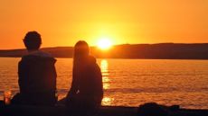 A couple watching the sun set across a bay