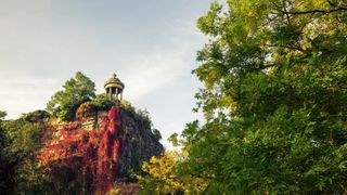 A stone pavilion can be seen from the lower part of a lush park right before sunset.