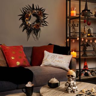 a halloween themed living room with light brown walls, brown coach with orange, black and white cushions, halloween, gonks and skull decorations on the coffee table and display unit next to the couch