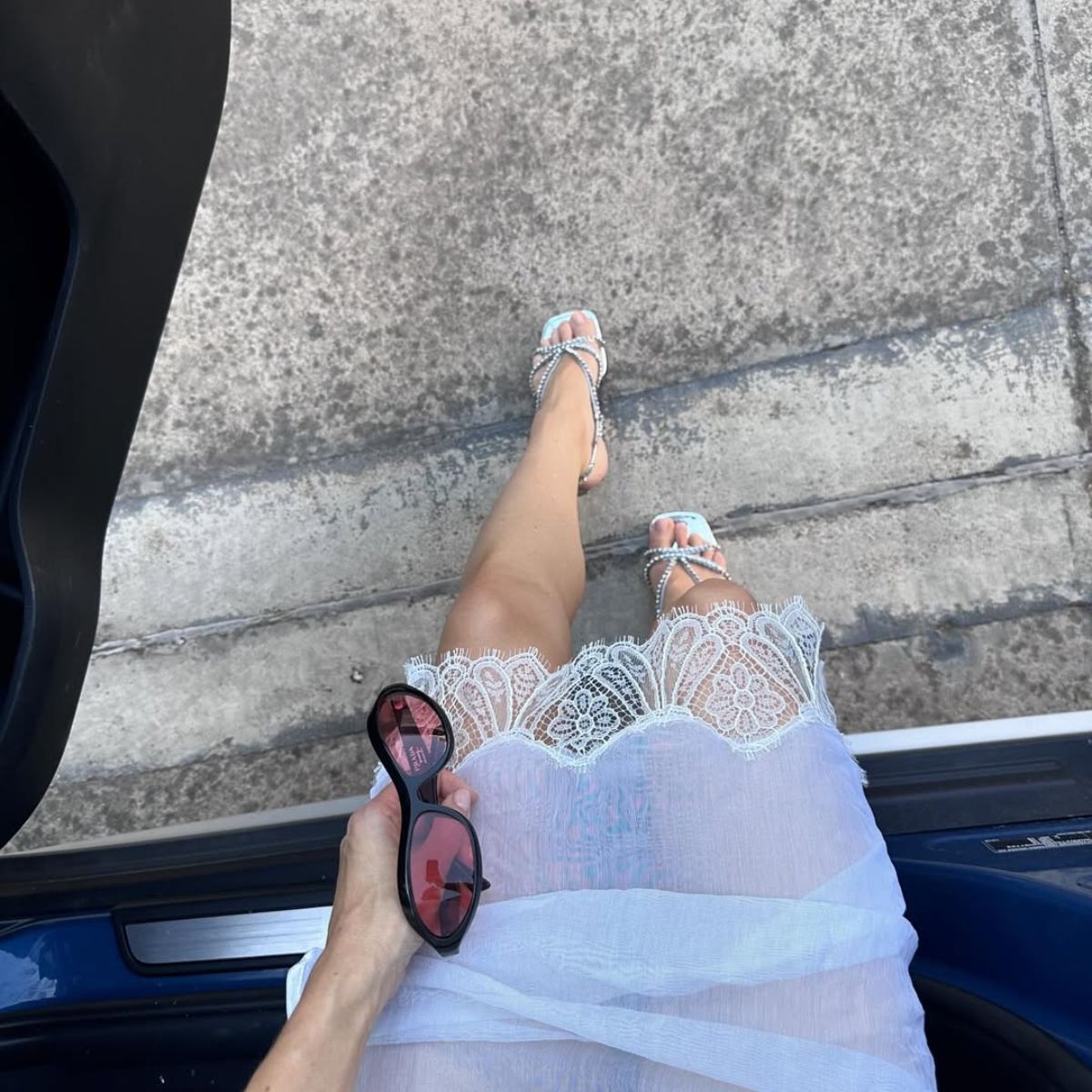 woman wearing lace skirt and sparkly sandals holding black sunglasses