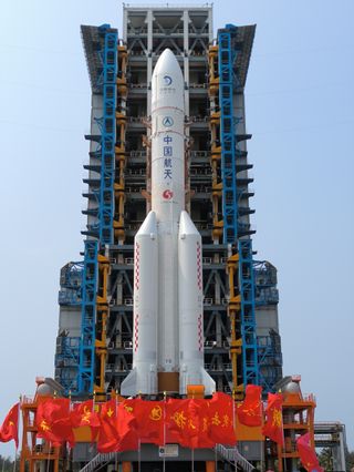 a large white rocket stands upright on a launch tower surrounded by red flags with yellow chinese characters