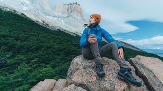 Hiker wearing waterproof jacket sitting on rocky outcrop