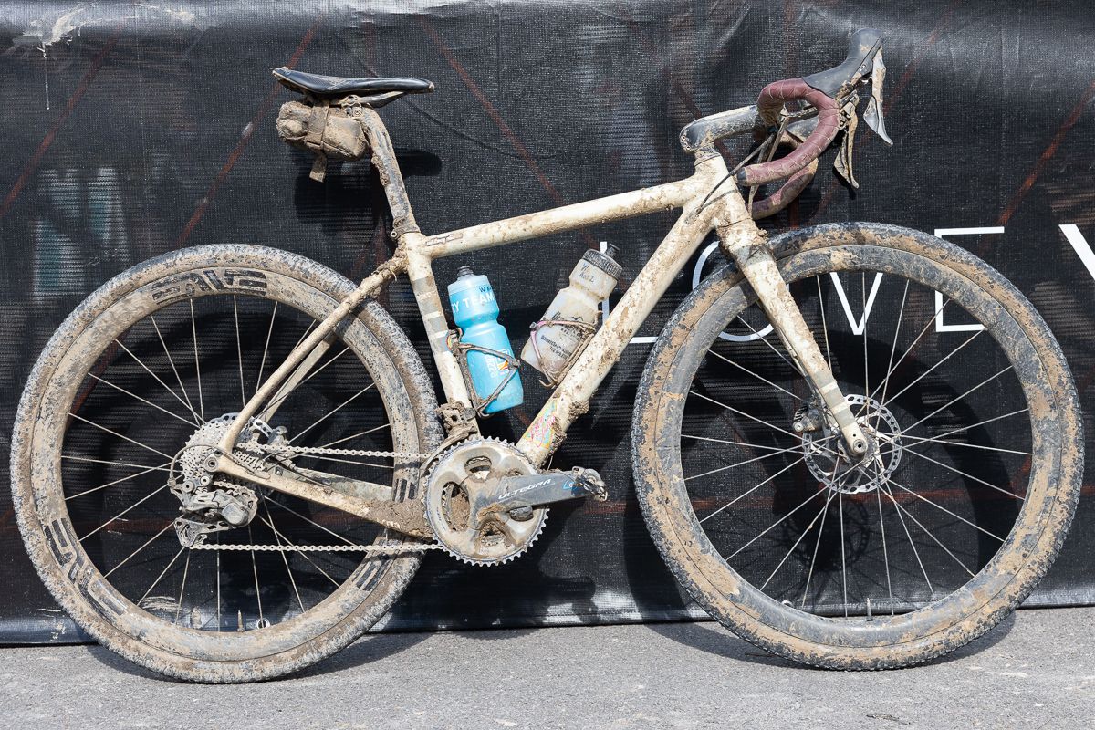 A muddy white gravel bike with red bar tape