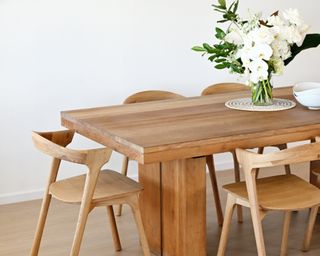 Clean wooden table and chairs, with white flowers in the middle of the table
