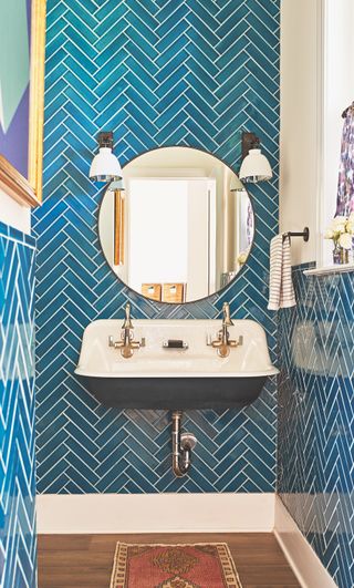 Μια παραδοσιακή λεκάνη μπροστά από έναν τοίχο μπάνιου με πλακάκια από μπλε ψαροκόκαλο και έναν καθρέφτη