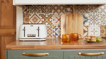 Kitchen with patterned backsplash, wooden worktop with green and white painted cabinetry, white toaster and accessories displayed on top