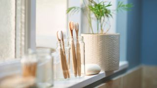 Bunch of wooden handled toothbrushes in jar sitting on shelf near the window
