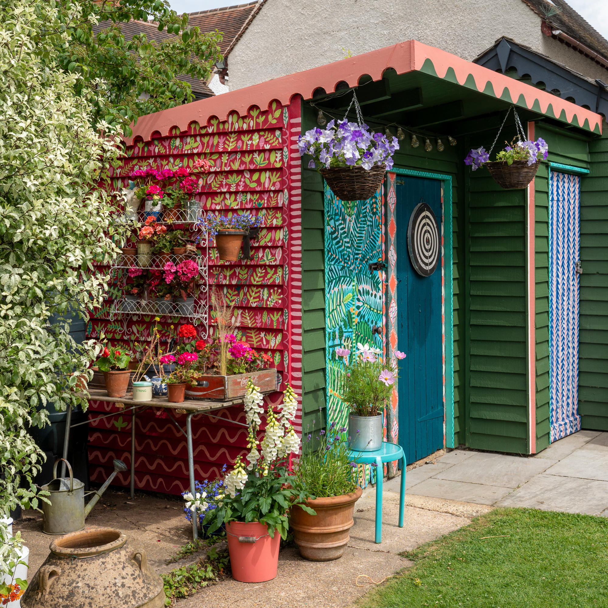 a brightly painted shed with planting around the side