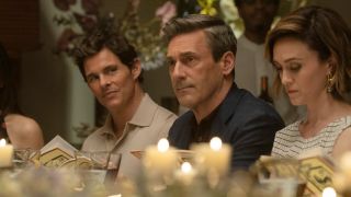 From left to right: James Marsden sitting at a table and looking to his right at Jon Hamm who is sitting right next to him. 